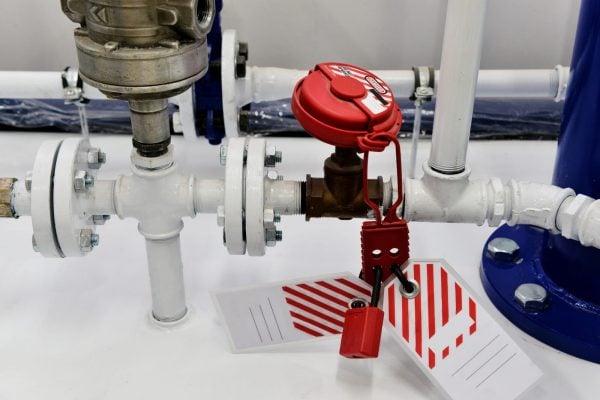 Red lockout tagout device and safety tags attached to an industrial pipe valve.